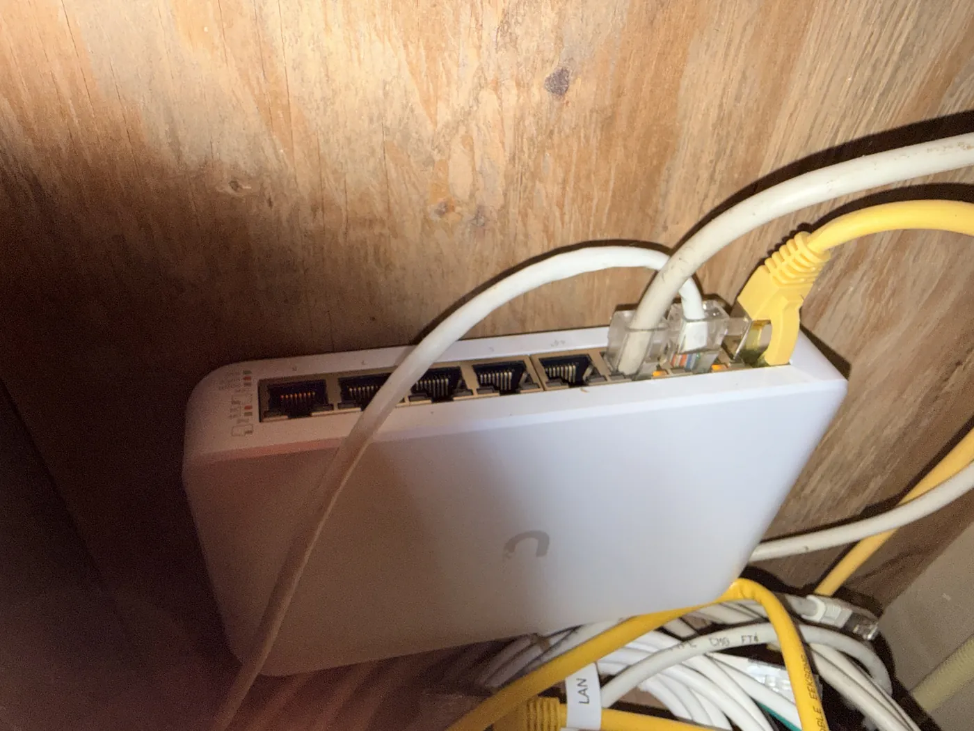 Een witte UniFi-switch tegen een houten wand met netwerkkabels