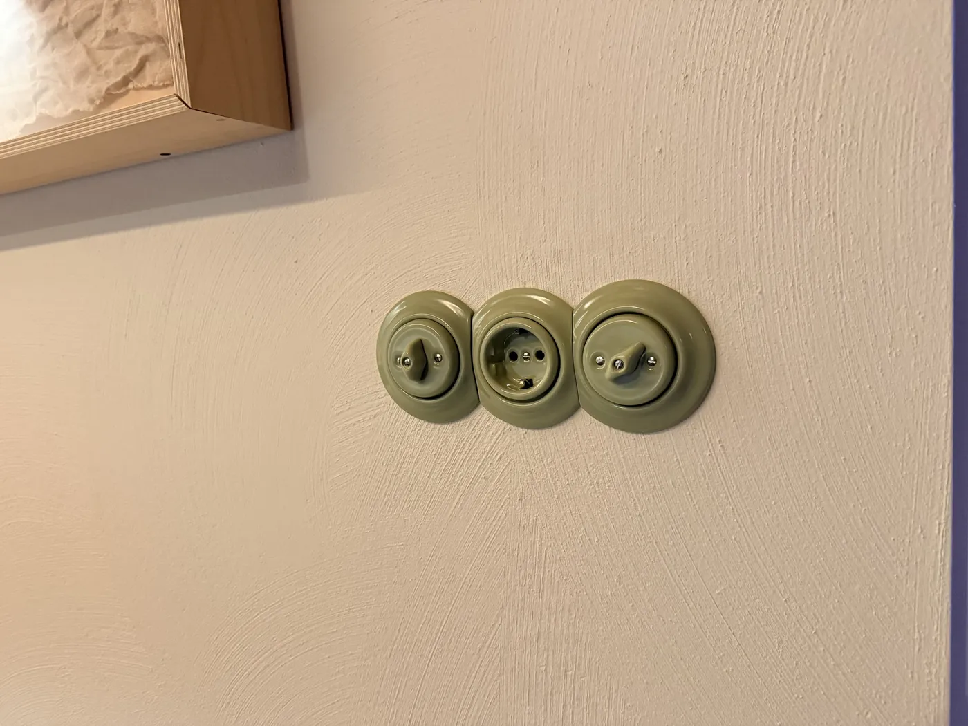 Drie saliegroene porseleinen schakelaars en een stopcontact van Katy Paty op een gestucte muur